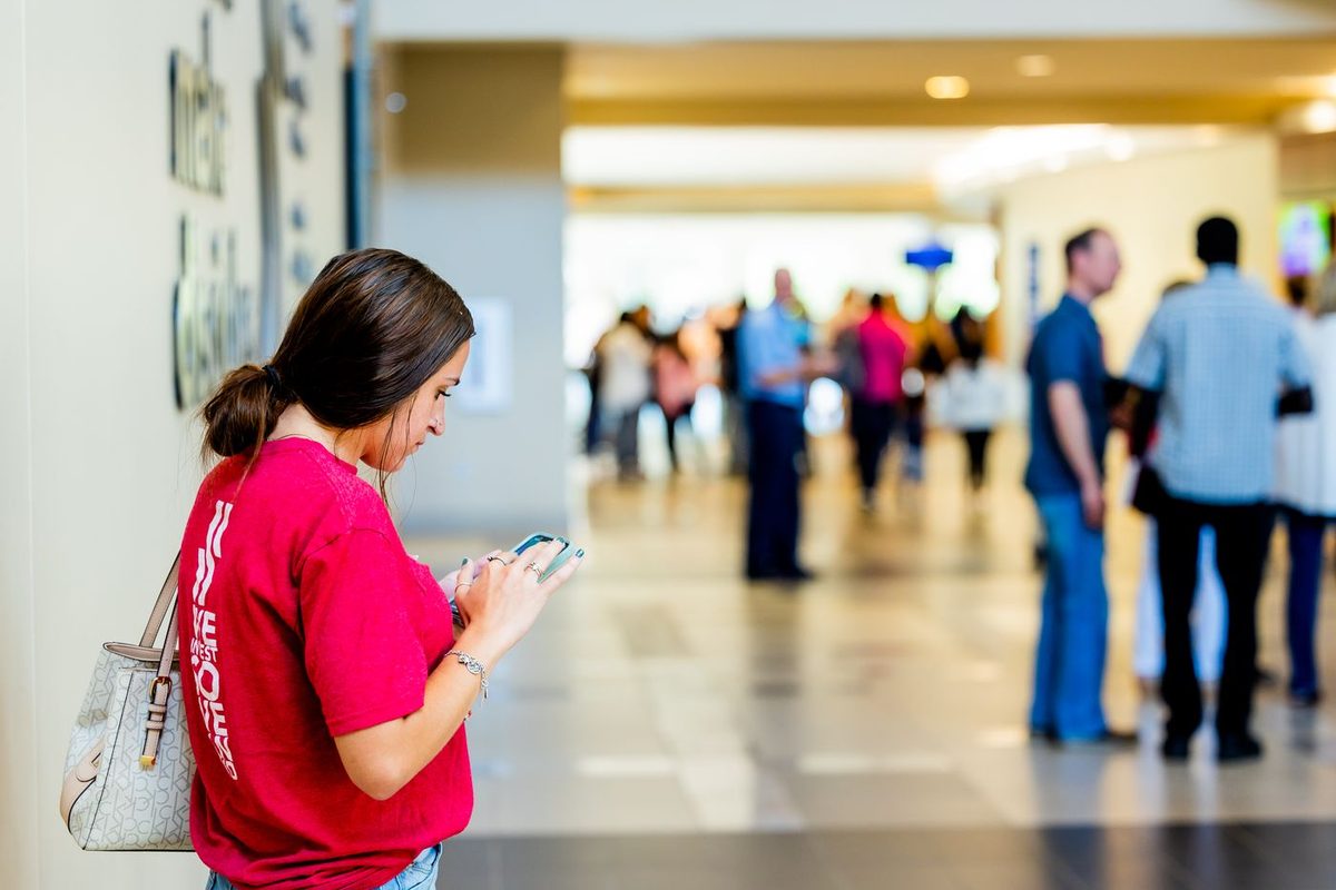 A shopper checking her phone in the concourse of a busy shopping centre